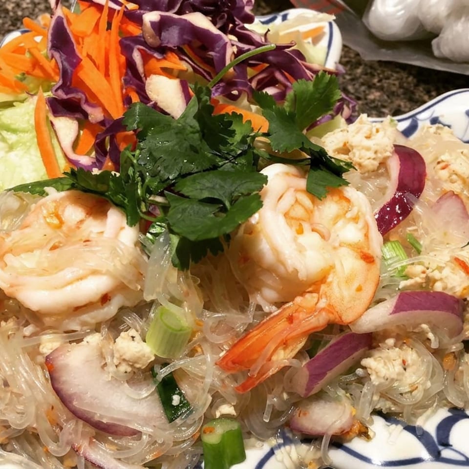 Thai-style glass noodle salad with shrimp, shredded vegetables, herbs, onions, and ground meat on a decorative plate.